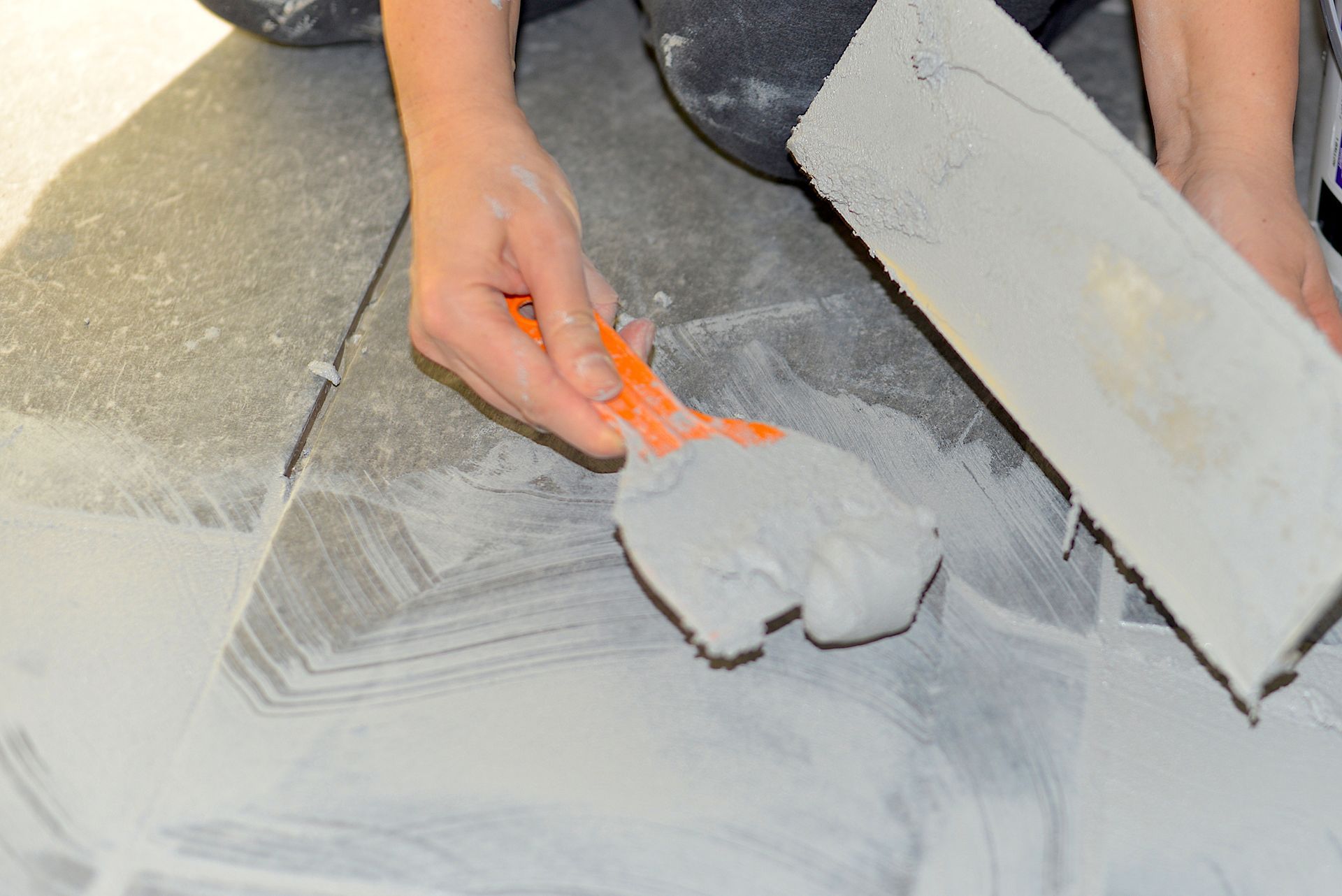 Person using a trowel and grout spreader to apply grout to floor tiles.