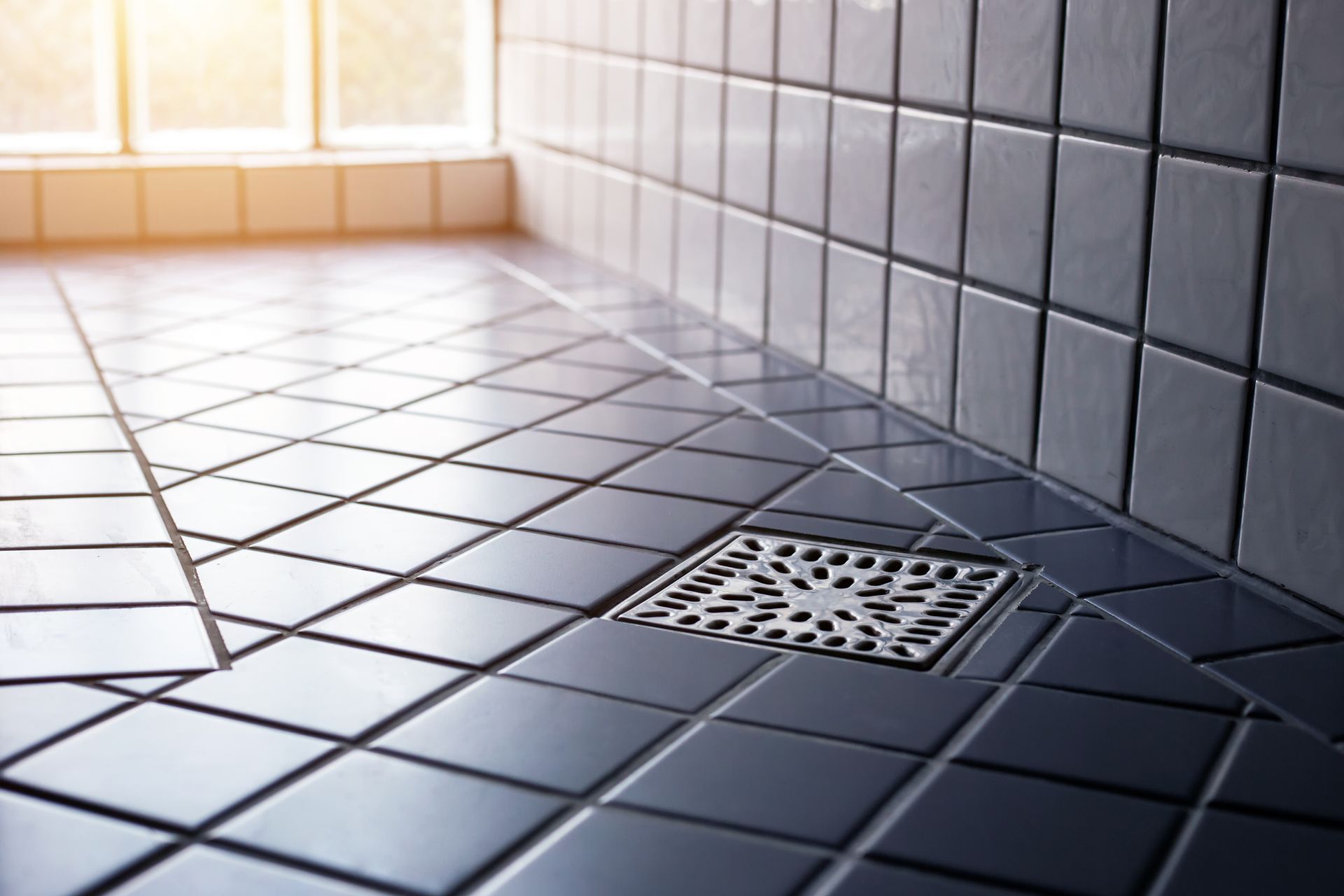 Dark blue tiled shower floor with a silver drain, near a window. Dark blue tiled shower floor with a silver drain, near a window.