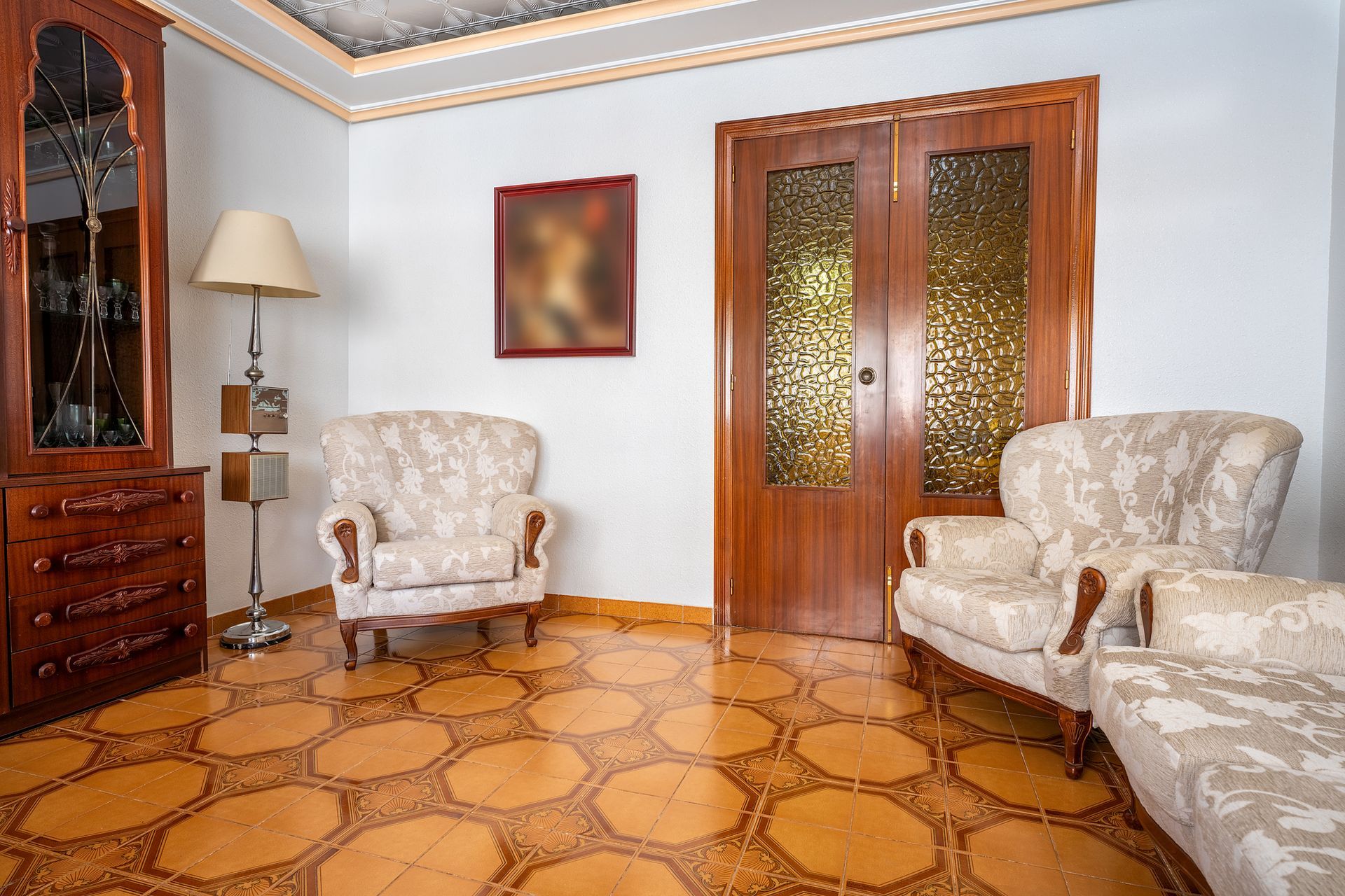 Living room with patterned floor, two armchairs, a cabinet, and wooden doors.