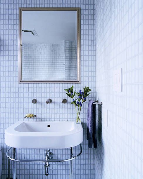 Light blue tiled bathroom with a wall-mounted sink, mirror, and a small vase of flowers.