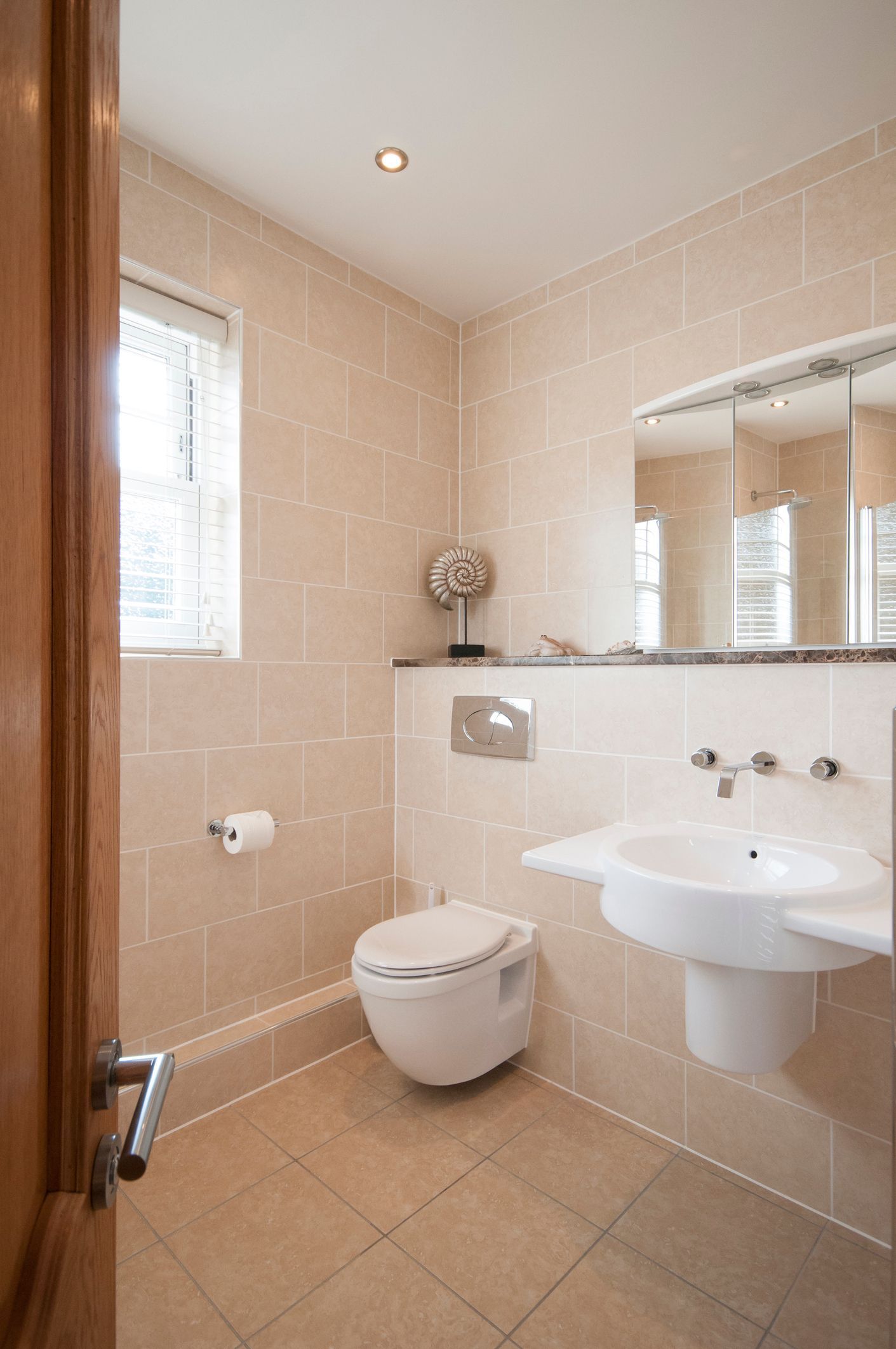 Bathroom with beige tiled walls, white fixtures, and a window with blinds.