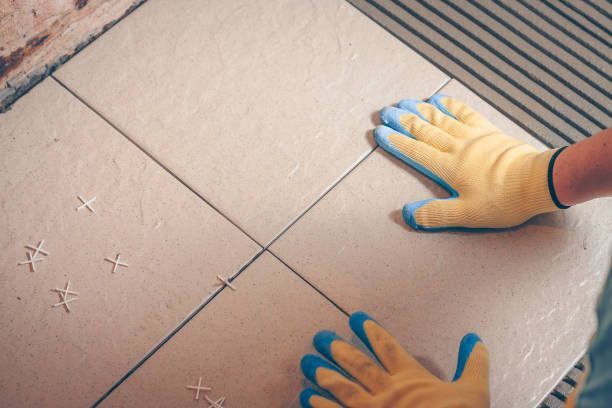 Person wearing gloves laying floor tiles, using spacers to align them.