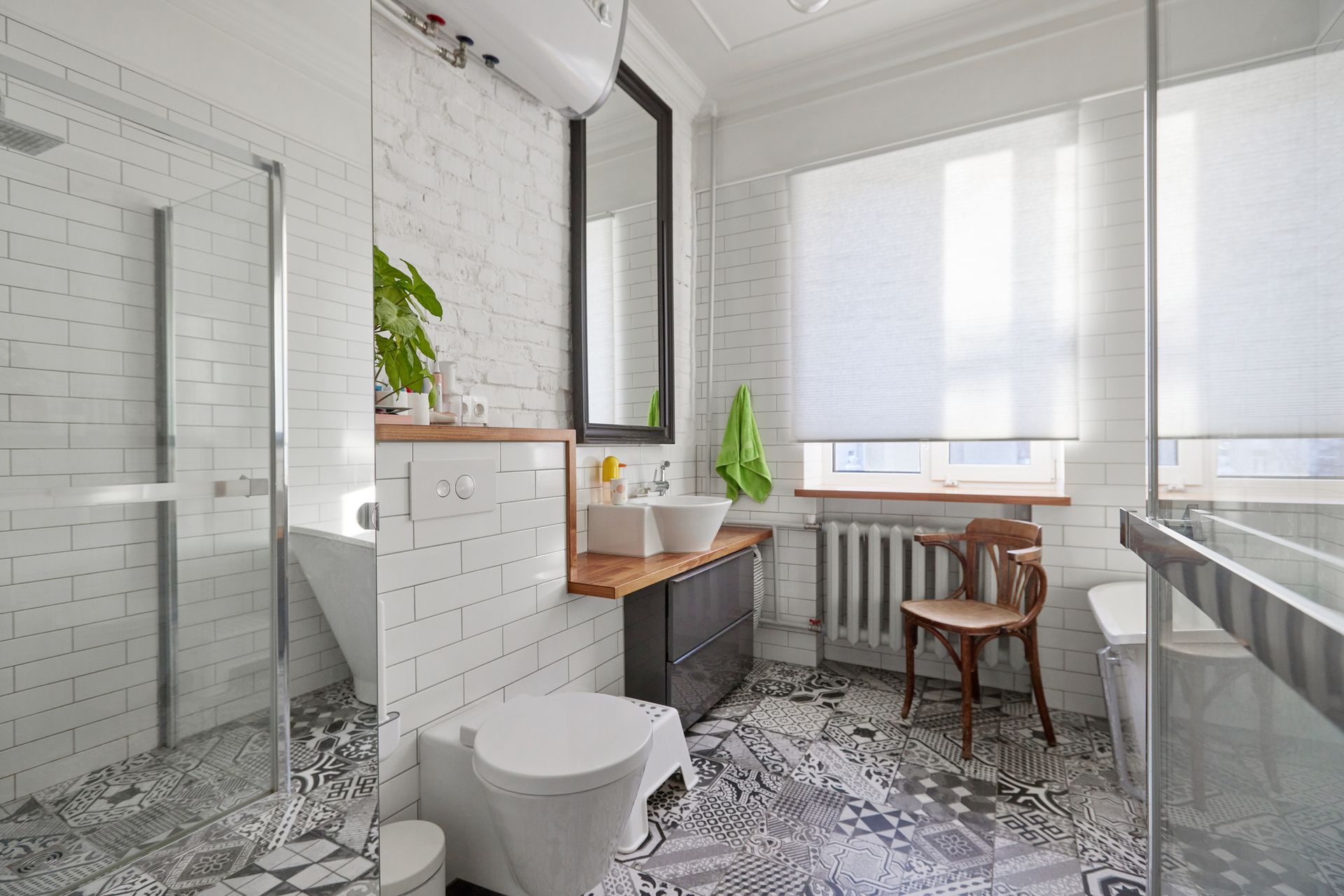 Bathroom with glass shower, white brick, patterned tile floor, window with blinds.