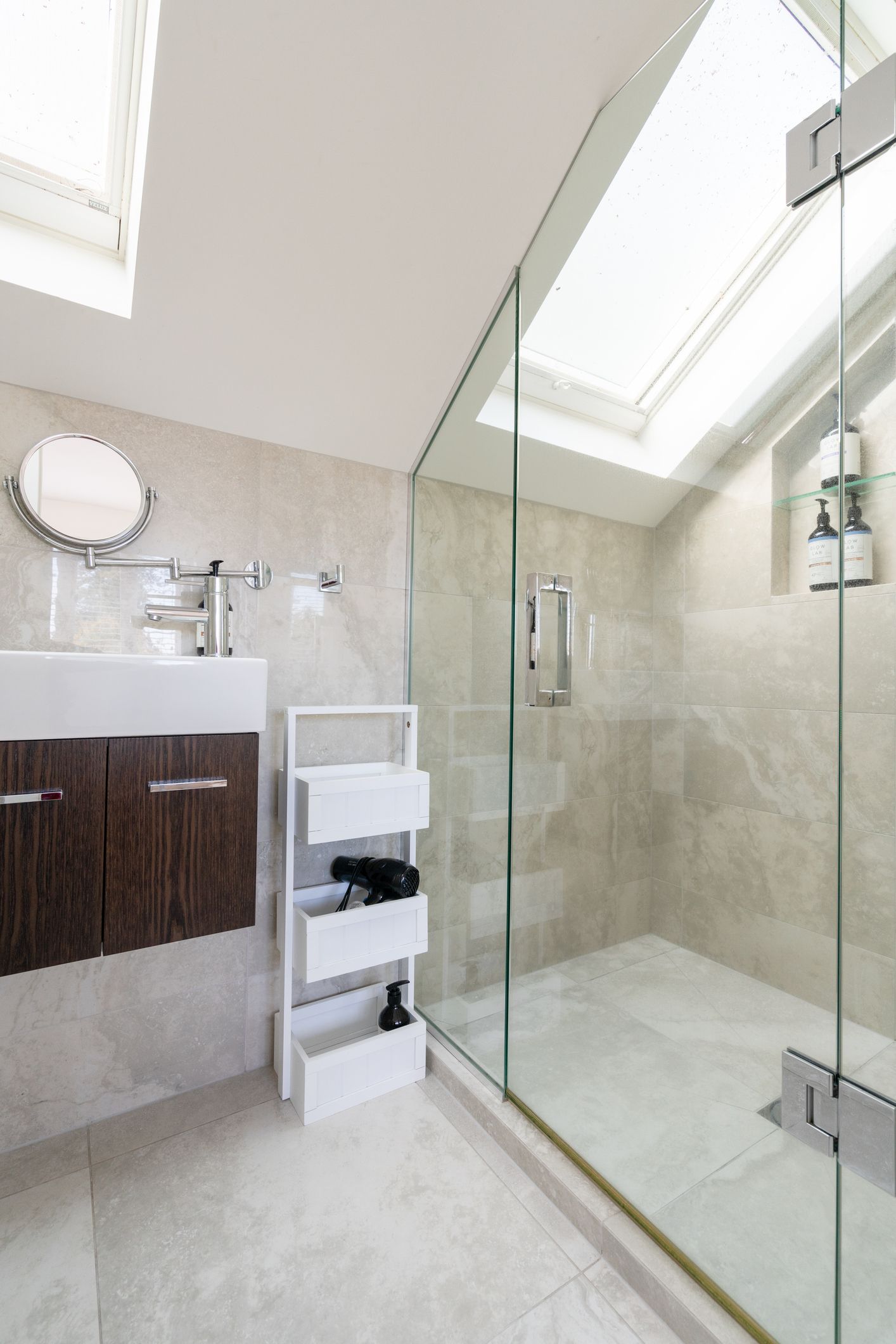 Modern bathroom with glass shower, white vanity, and skylight.