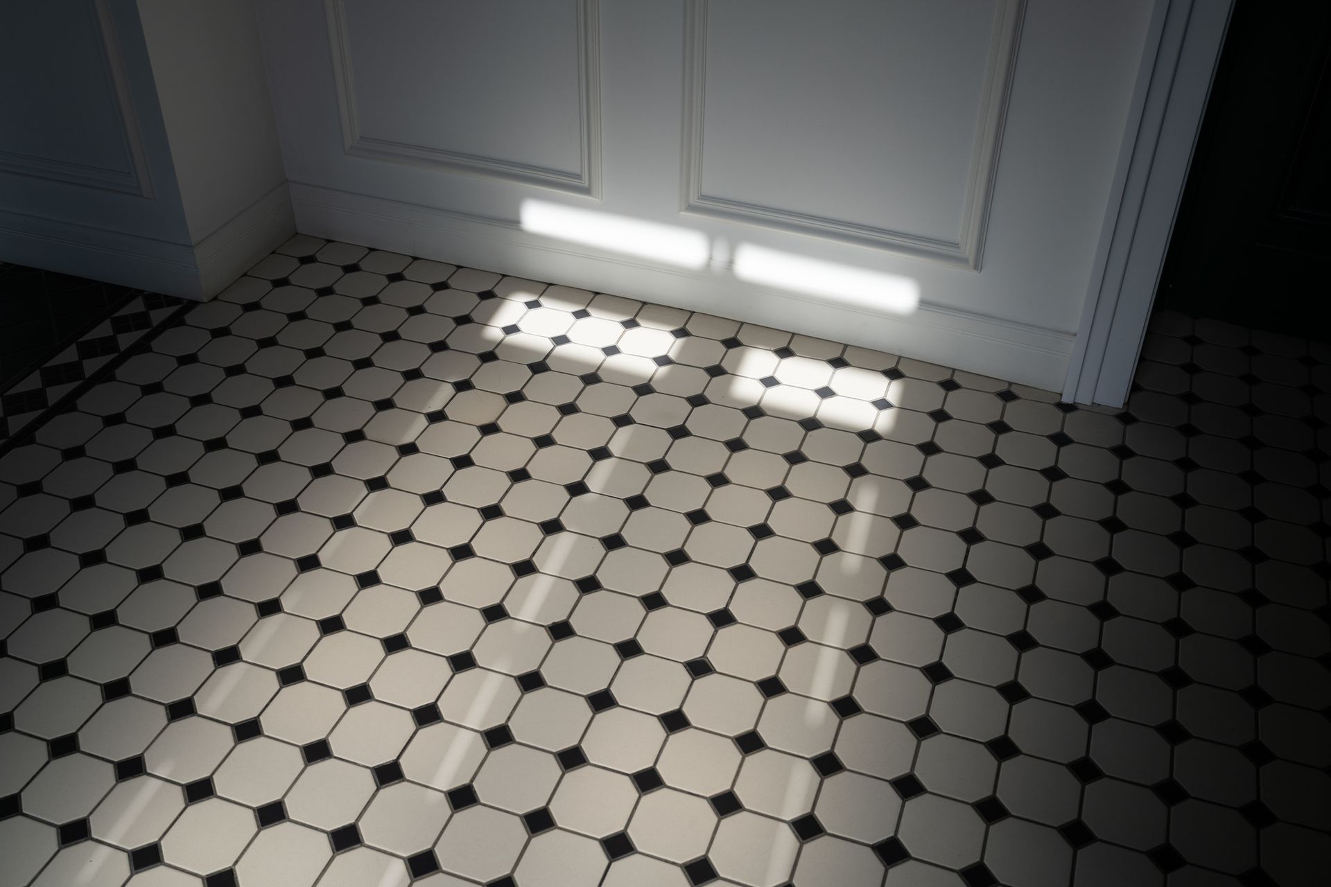 Tiled floor with black and white octagonal tiles. Light from the door creates rectangular patches on the floor.
