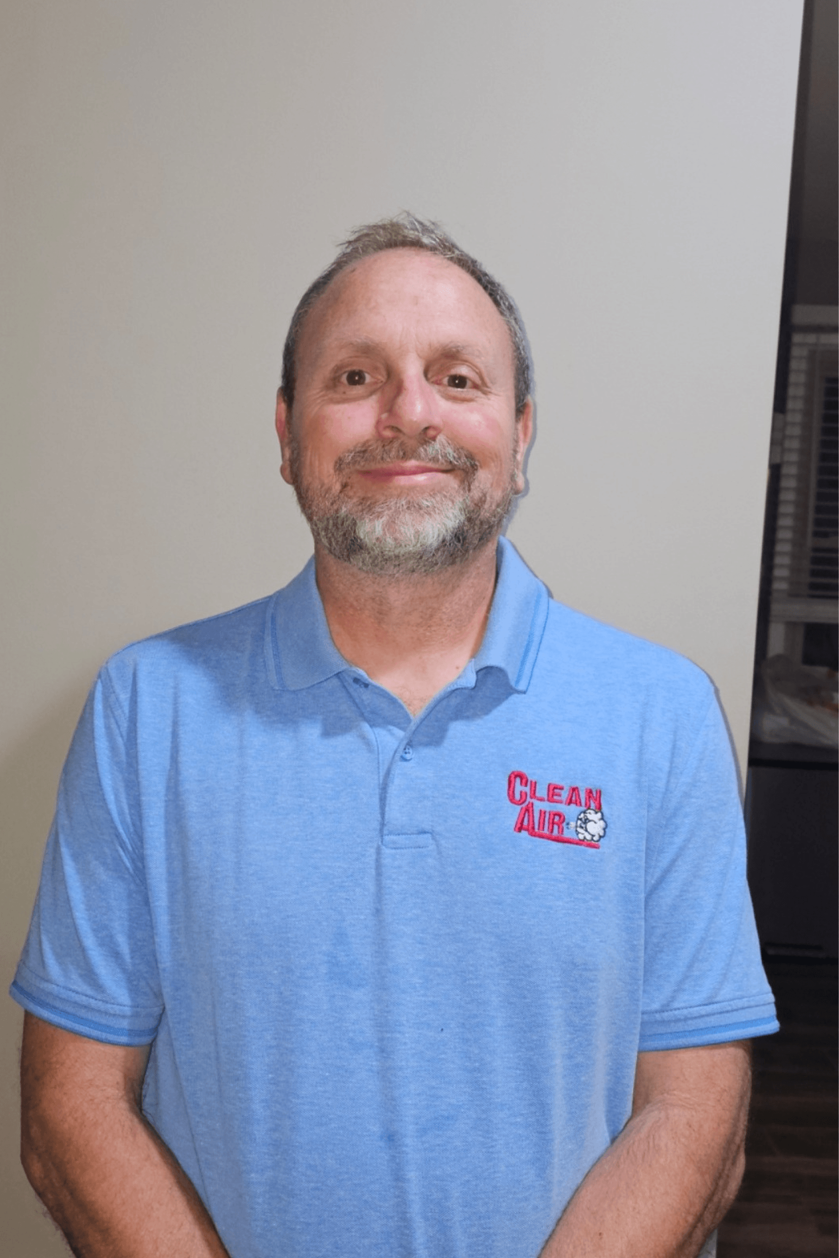 A man with a beard is wearing a blue polo shirt and smiling.