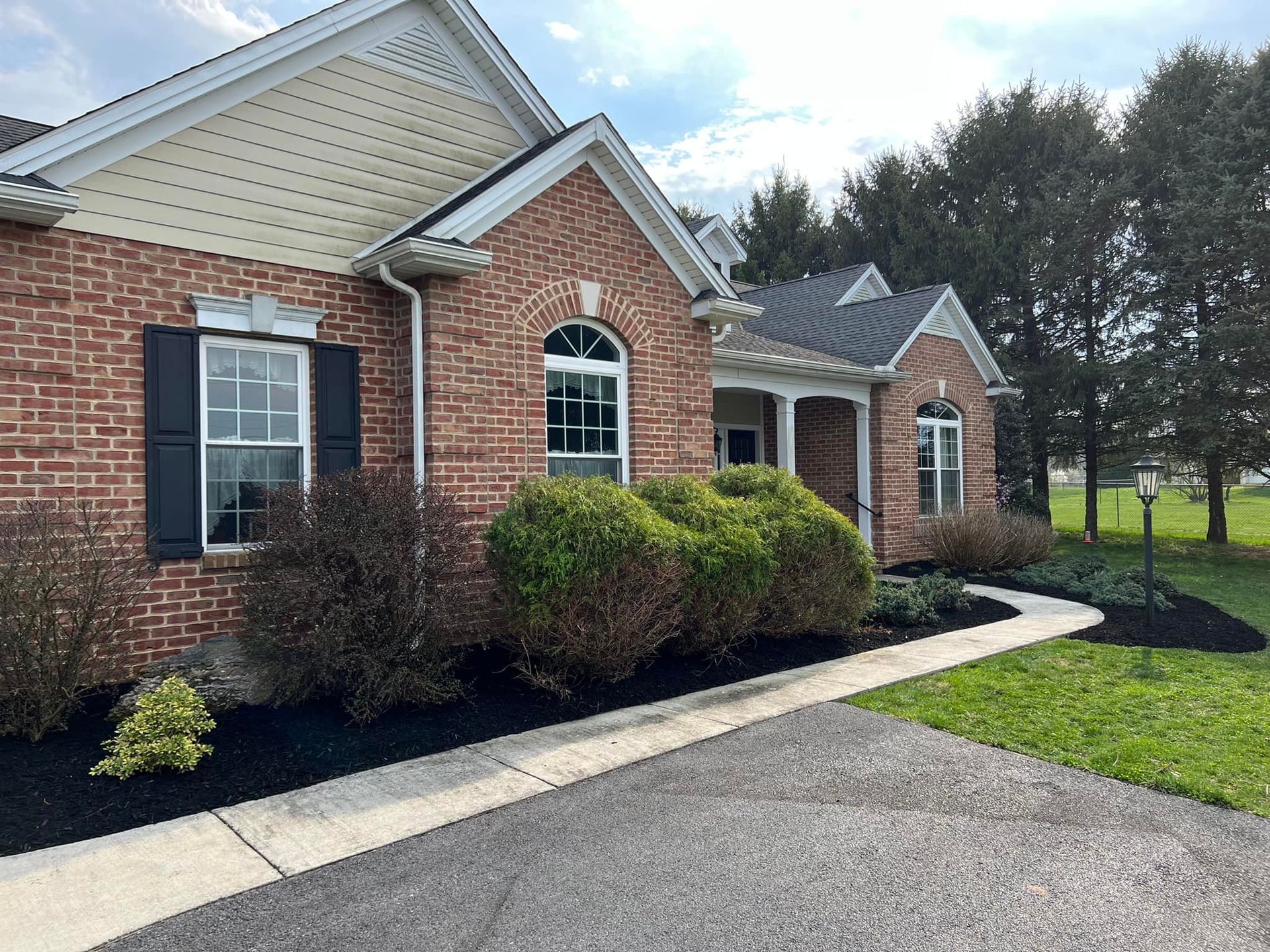 A brick house with black shutters and a walkway leading to it.