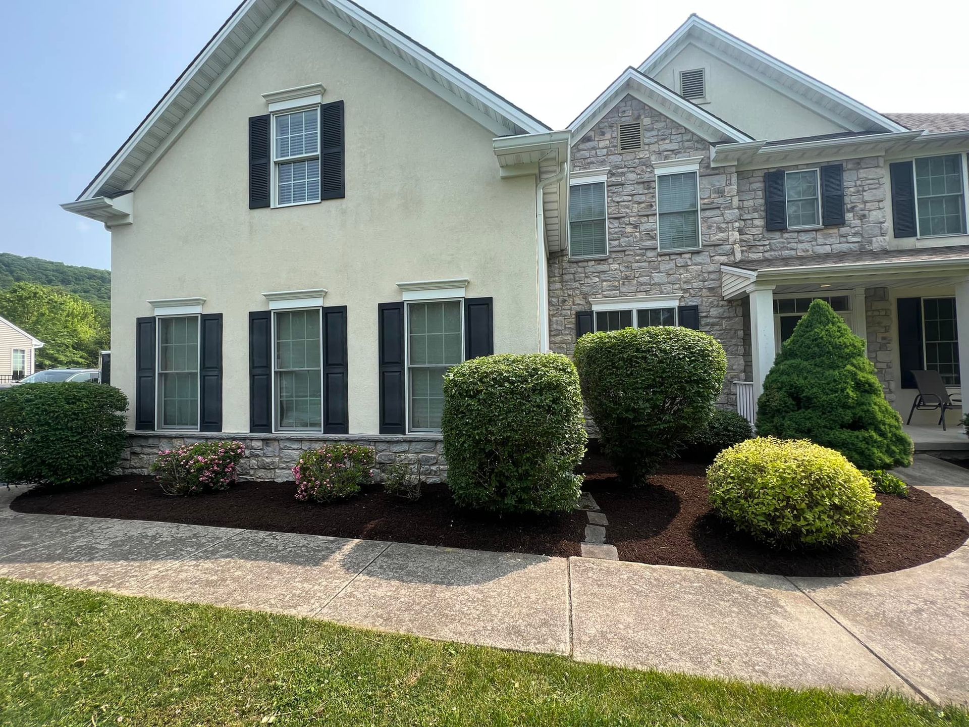 A large white house with black shutters and bushes in front of it.