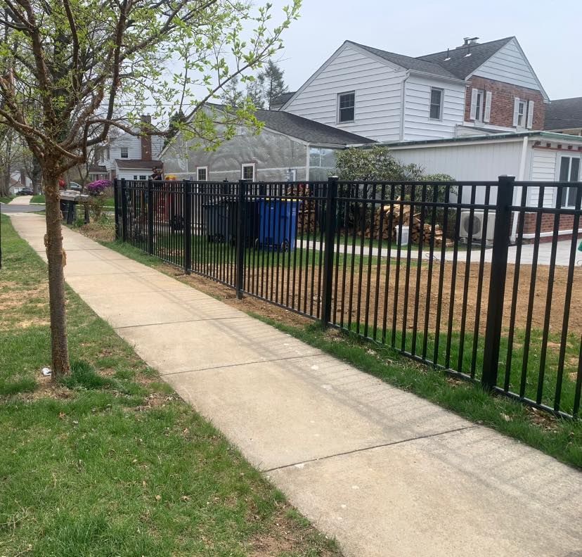 A sidewalk next to a fence with a house in the background.