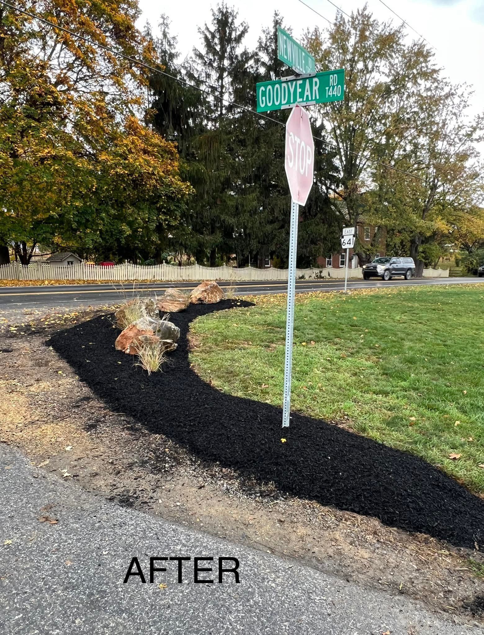 A street sign is sitting on the side of a road next to a grassy area.