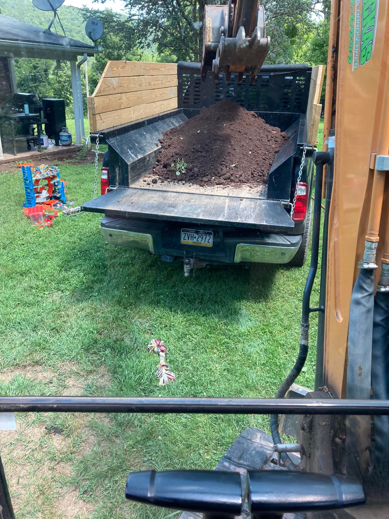 A dump truck is being loaded with dirt in a backyard.