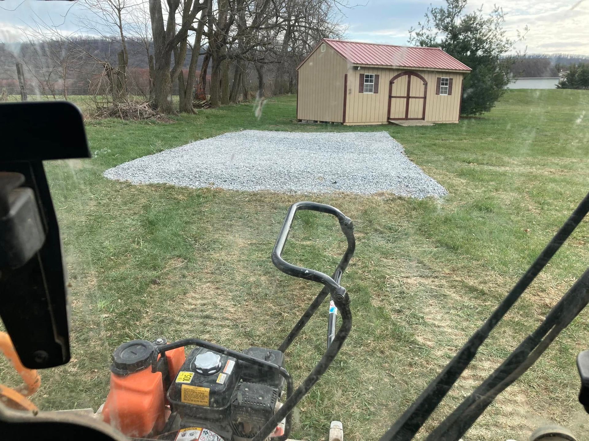 A person is driving a tractor in a field with a shed in the background.