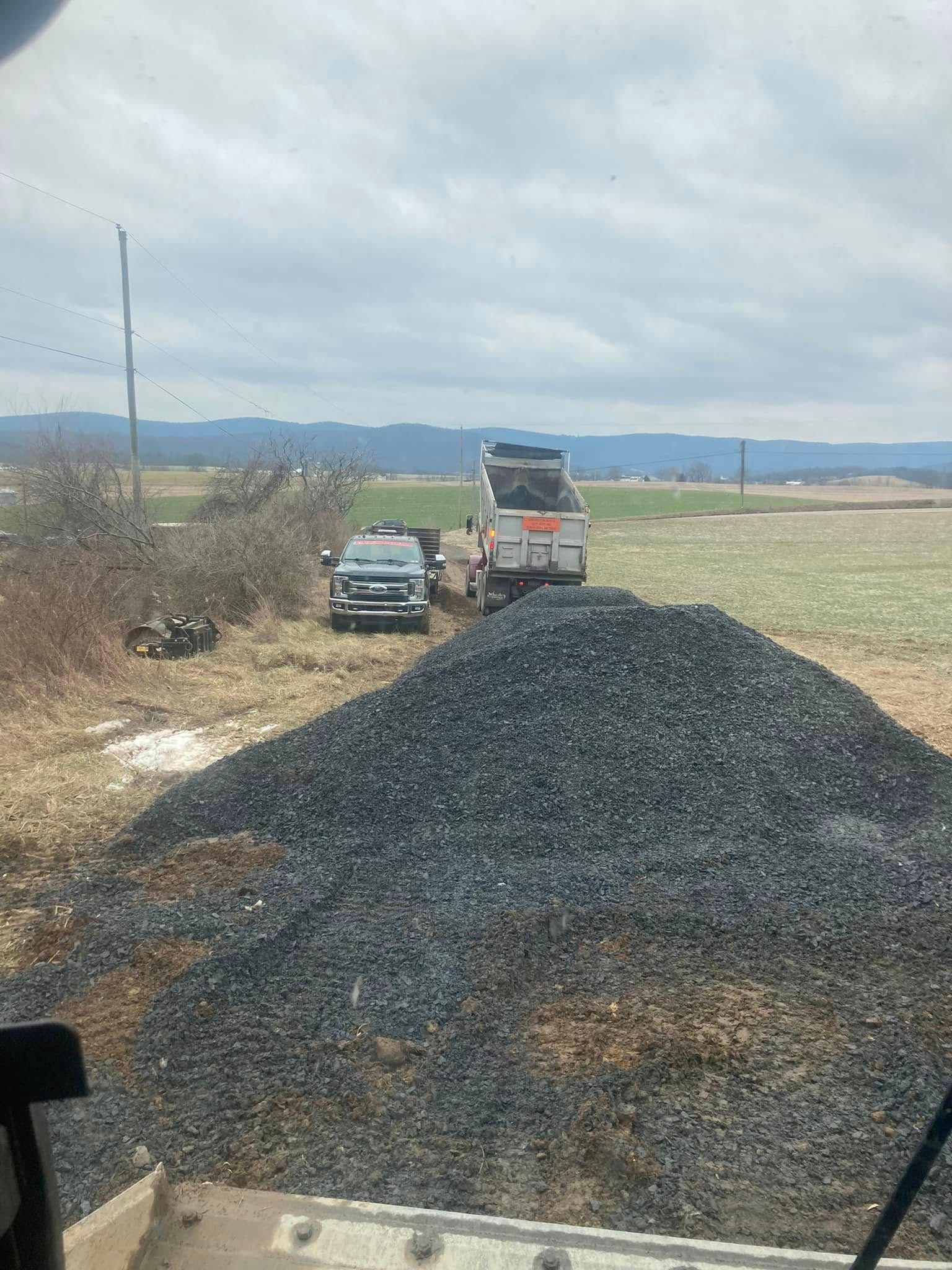 A truck is driving down a dirt road next to a pile of gravel.