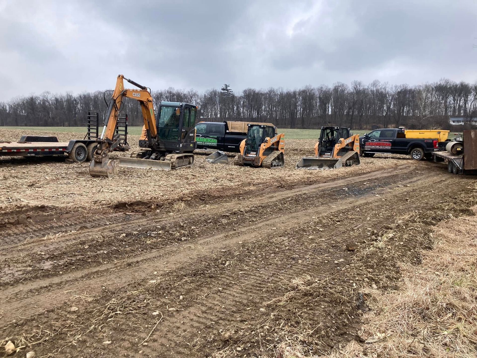 A row of construction vehicles are parked in a dirt field.