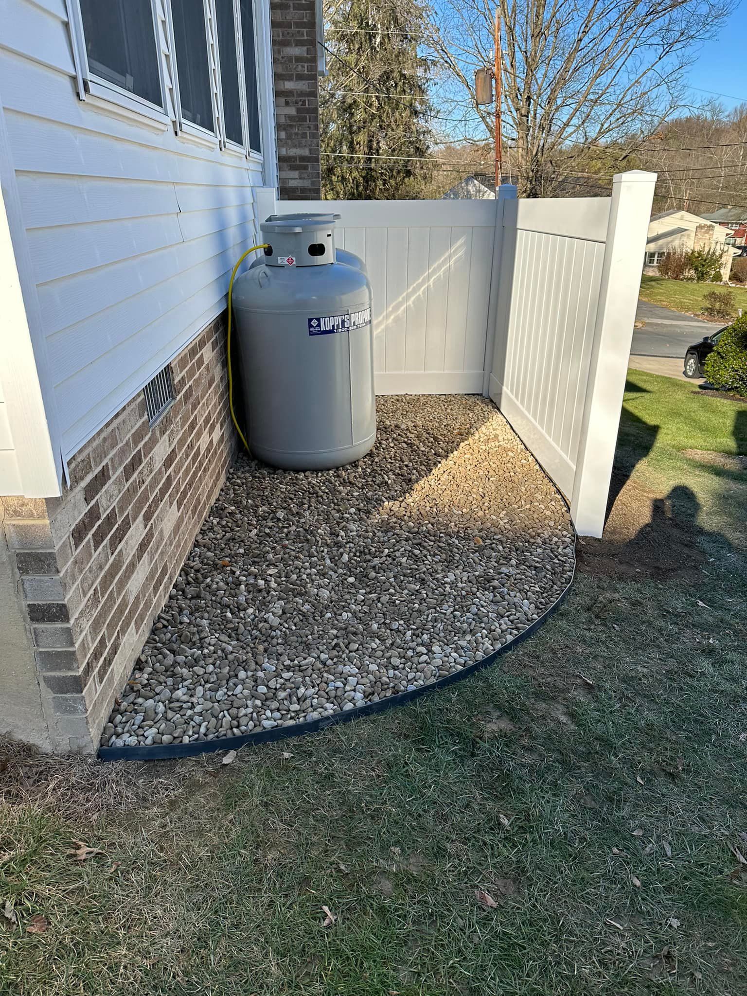 A propane tank is sitting on the side of a house next to a white fence.