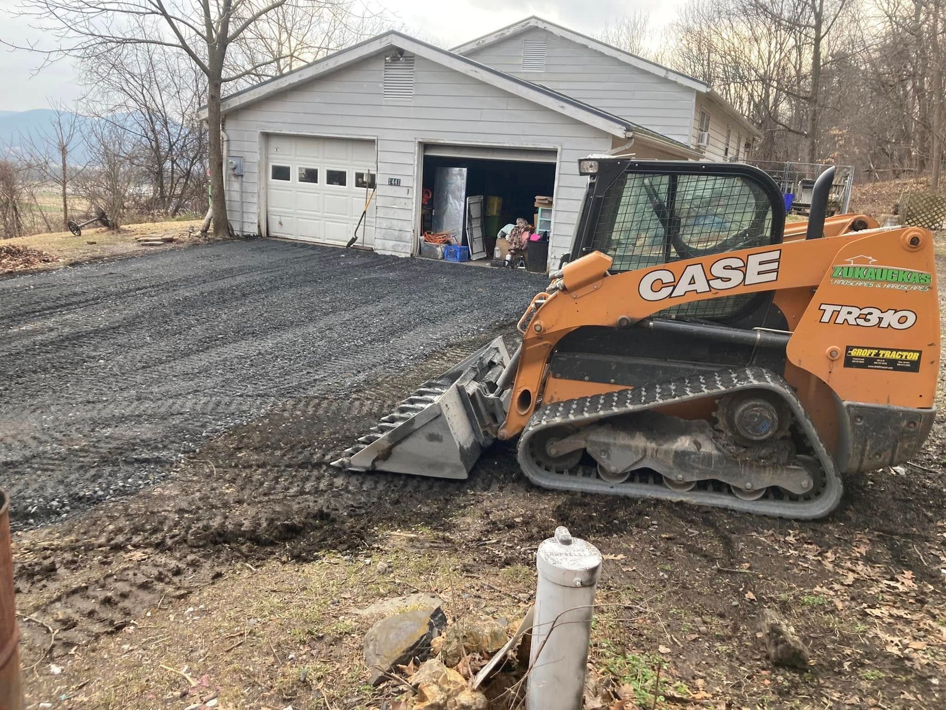 A case track loader is moving dirt in front of a garage.