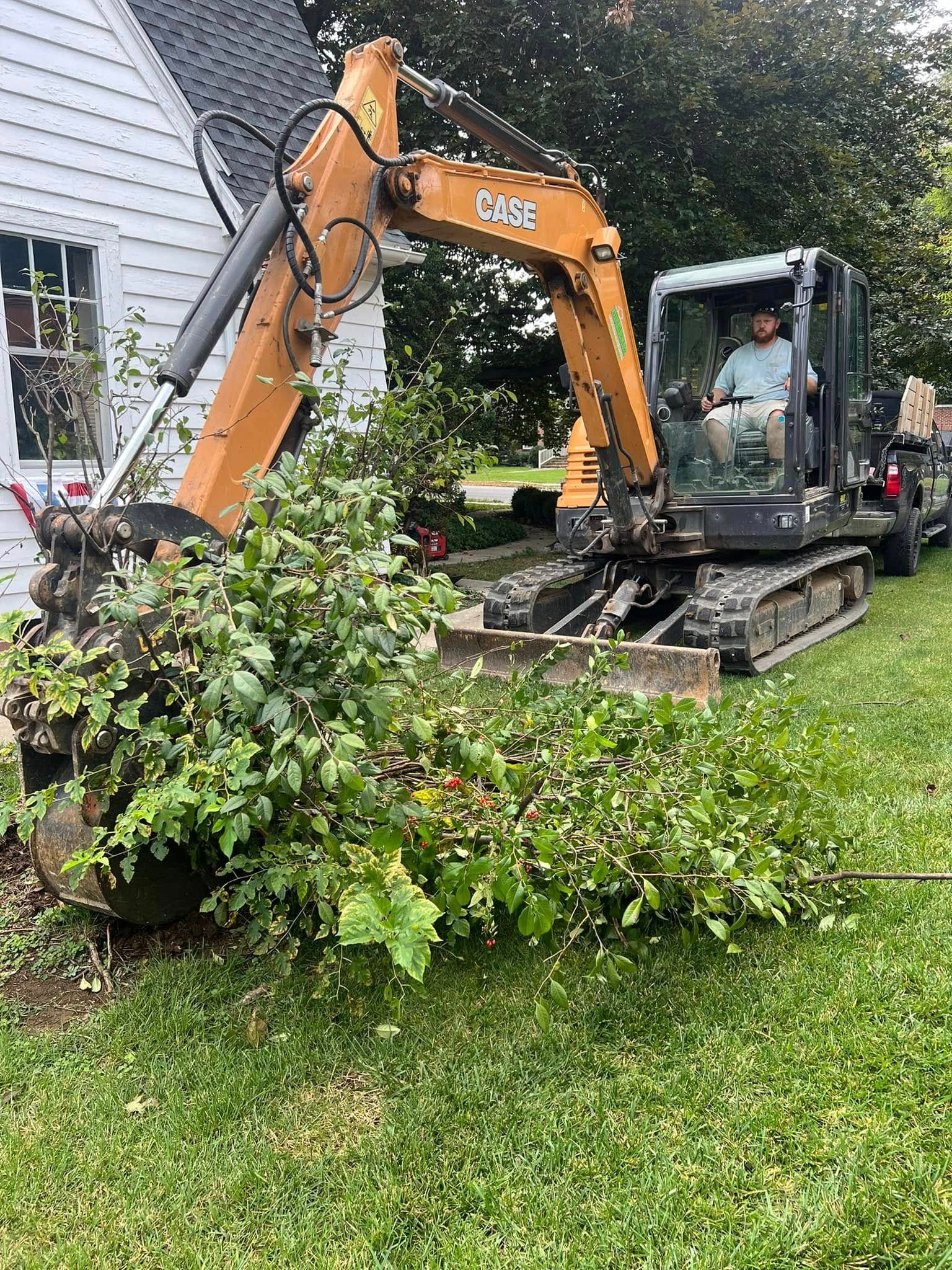 A man is driving an excavator in a yard next to a house.