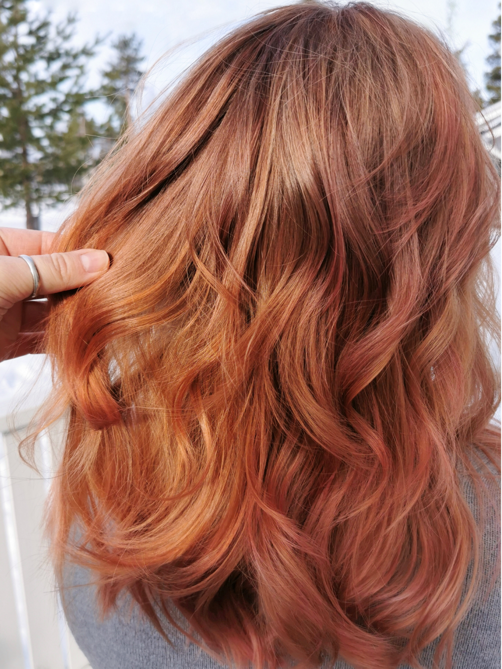 A woman with long red hair is holding her hair in her hand.