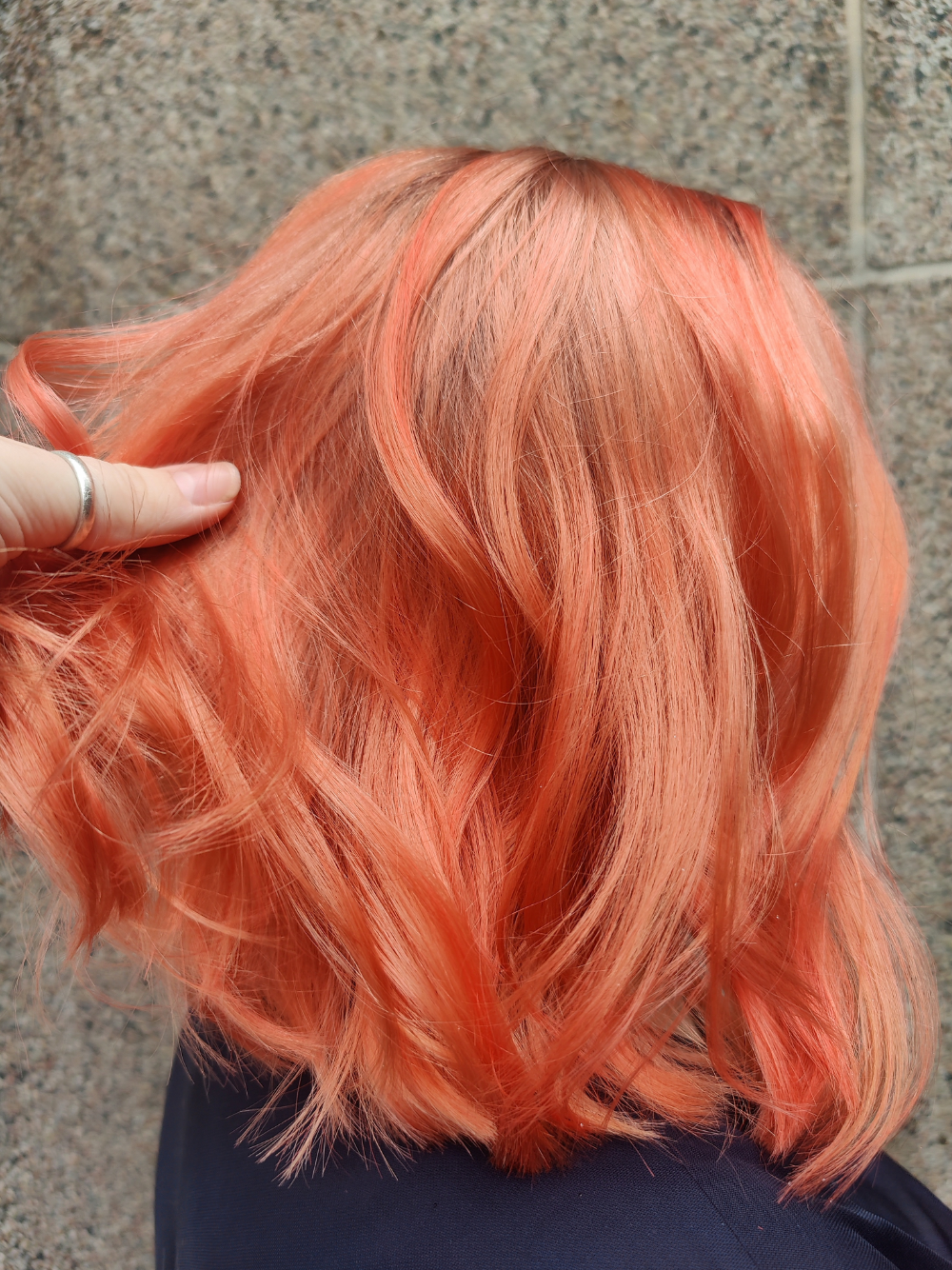 A woman with bright orange hair is standing in front of a wall.