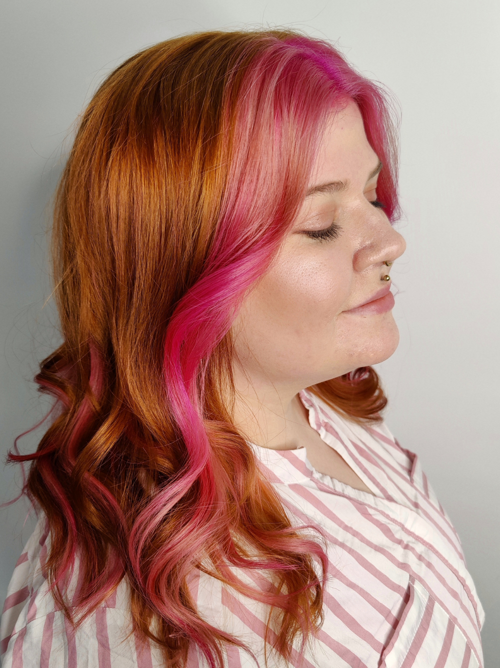 A woman with red hair and pink highlights is wearing a striped shirt.