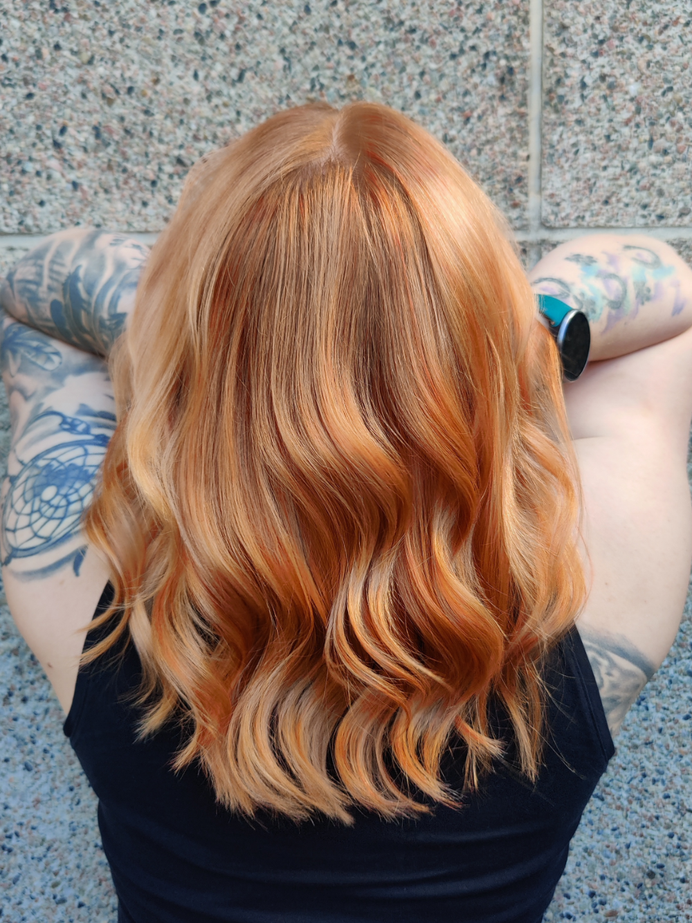 A woman with red hair and tattoos is sitting in front of a wall.