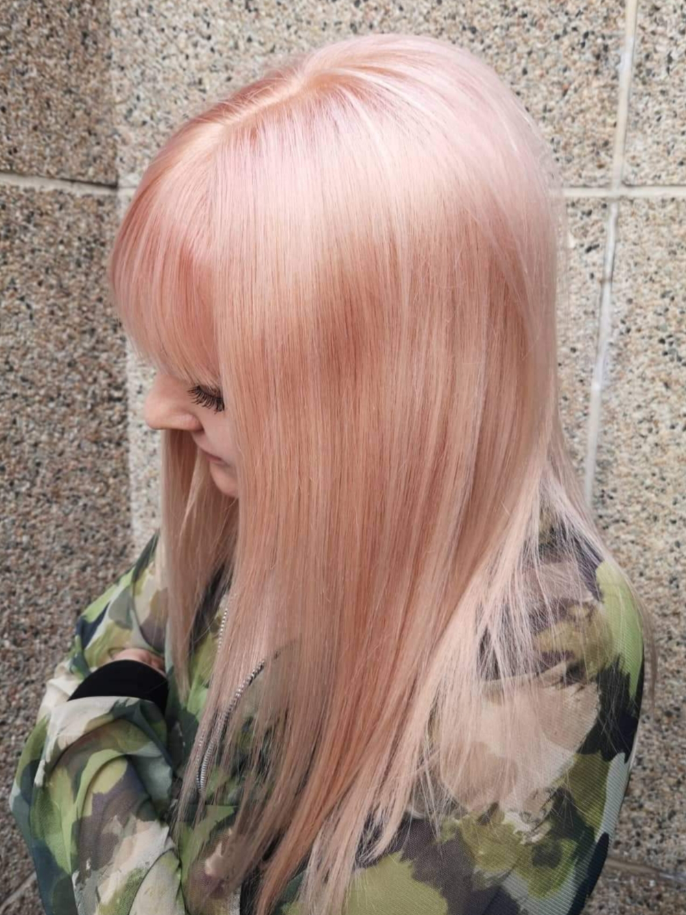 A woman with long pink hair is wearing a camouflage jacket.