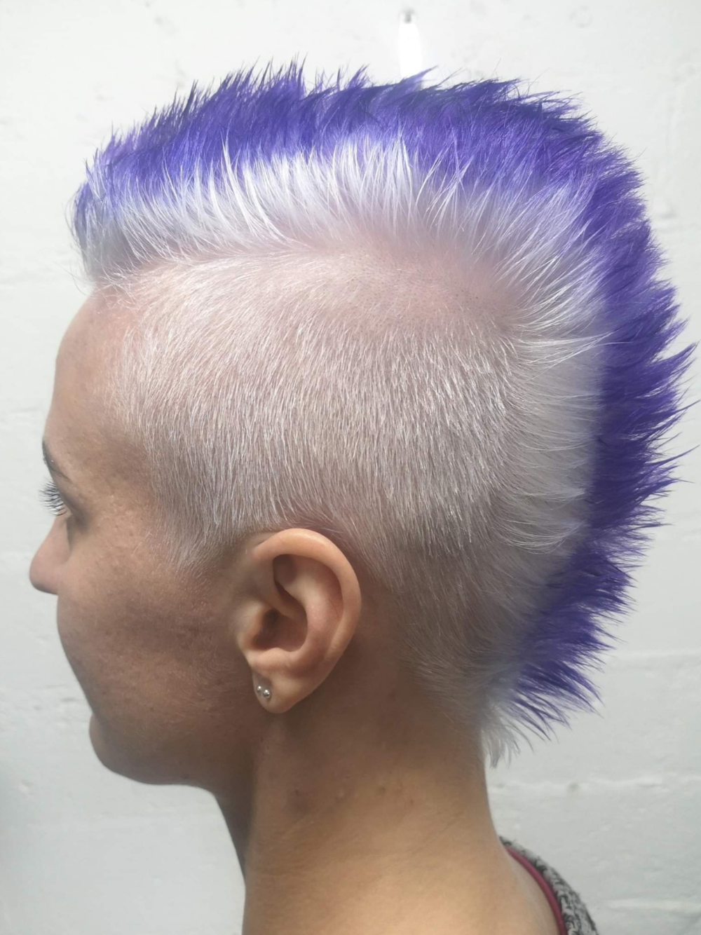 A woman with purple and white hair has a mohawk hairstyle.