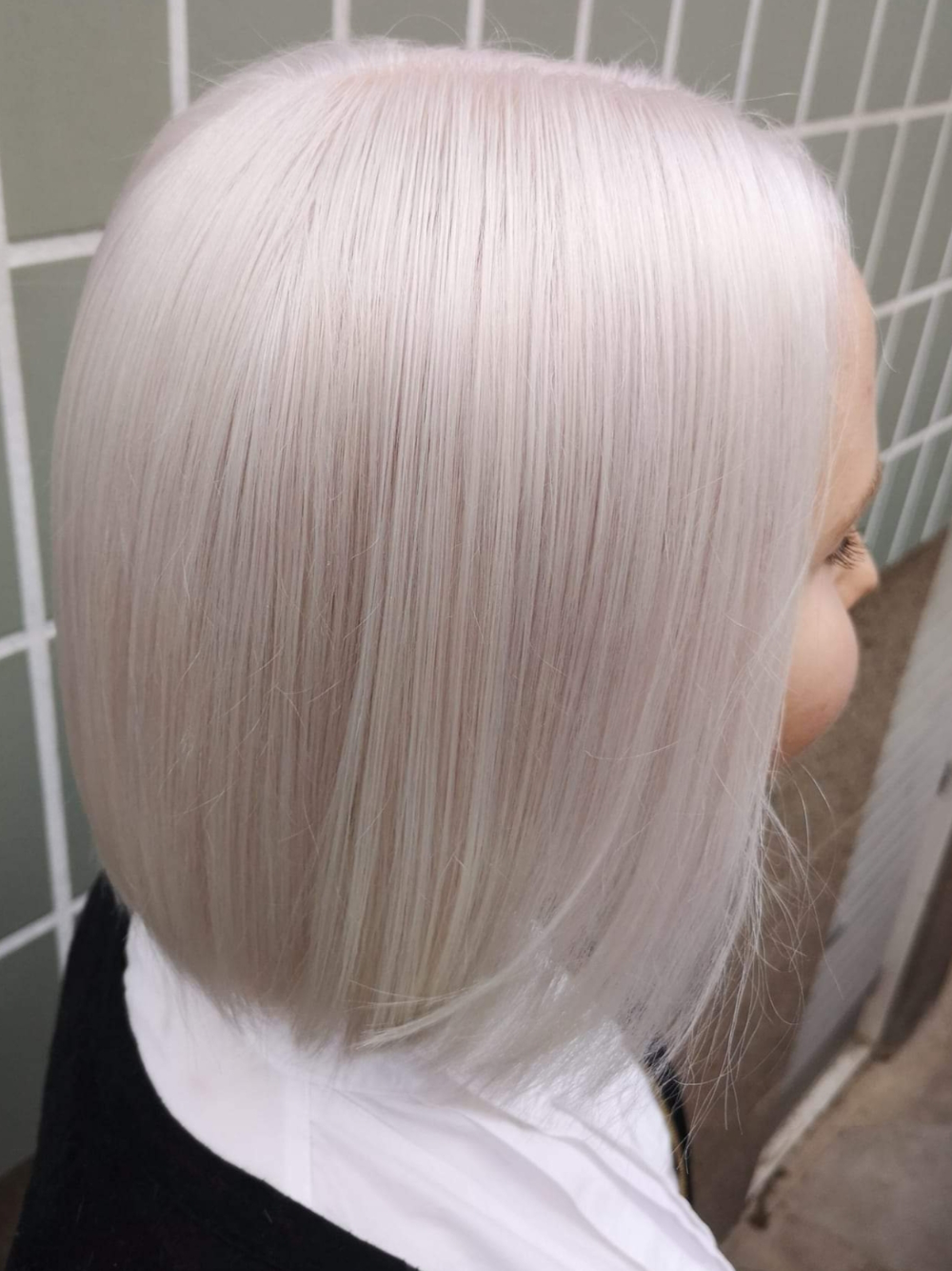 A woman with short white hair is standing in front of a tiled wall.