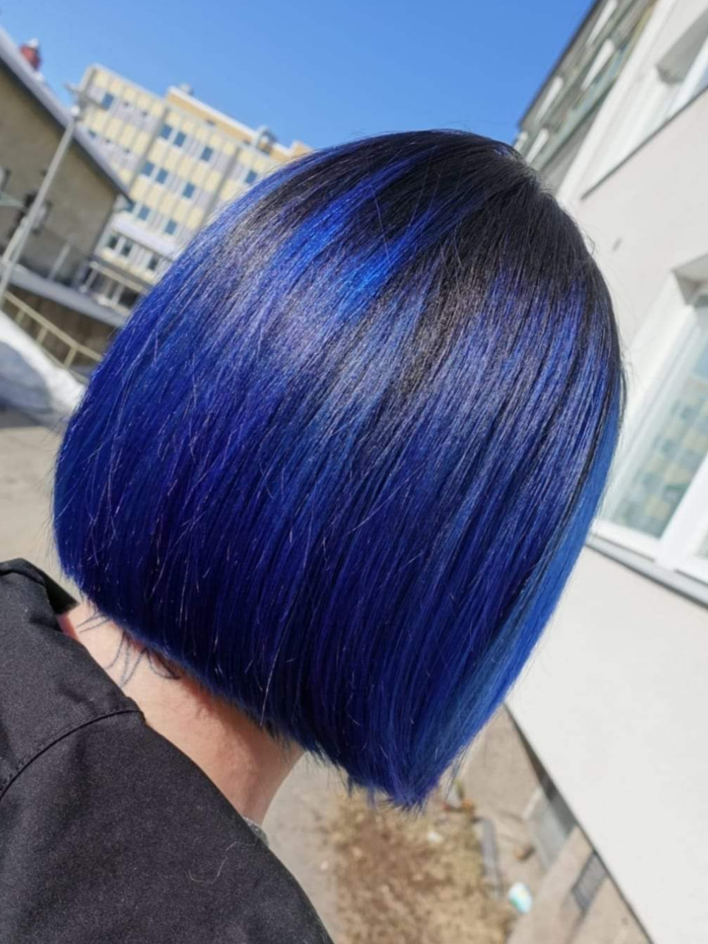 A woman with blue hair is standing in front of a building.