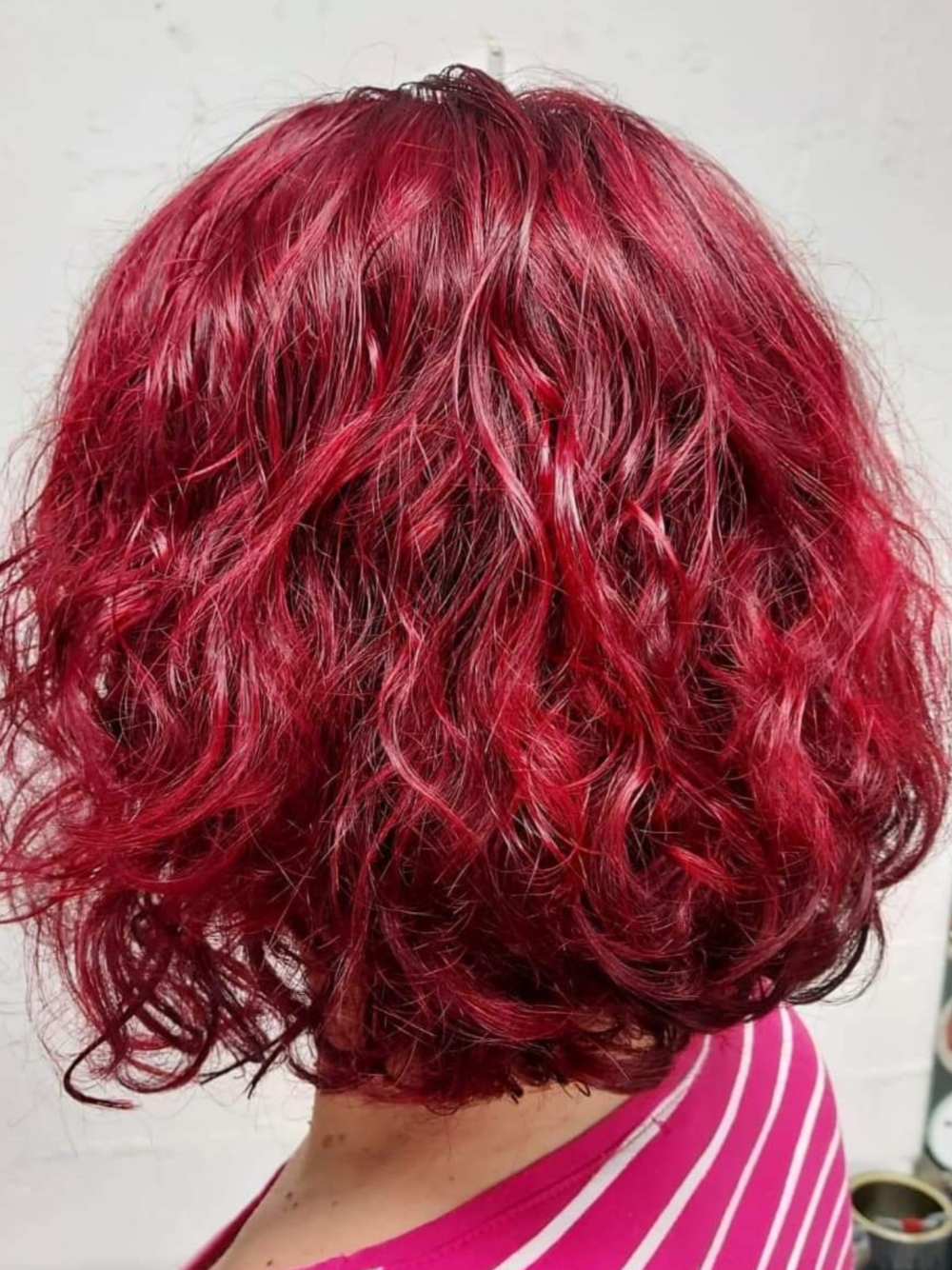 A woman with red curly hair is wearing a pink and white striped shirt.