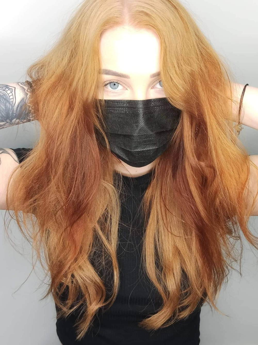 A woman with long red hair is wearing a black mask.