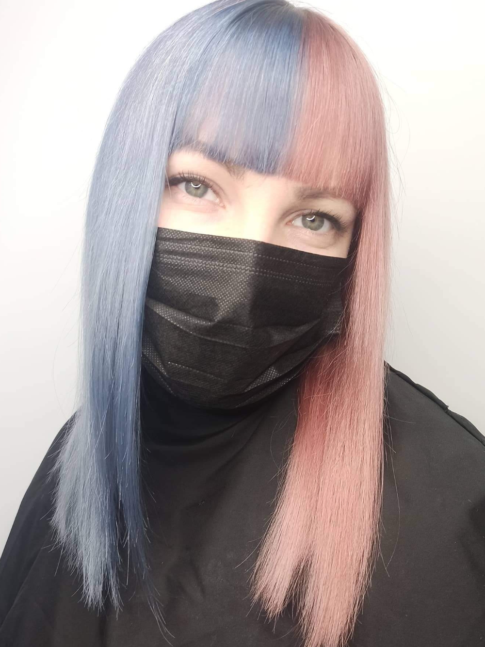 A woman with blue and pink hair is wearing a black mask.