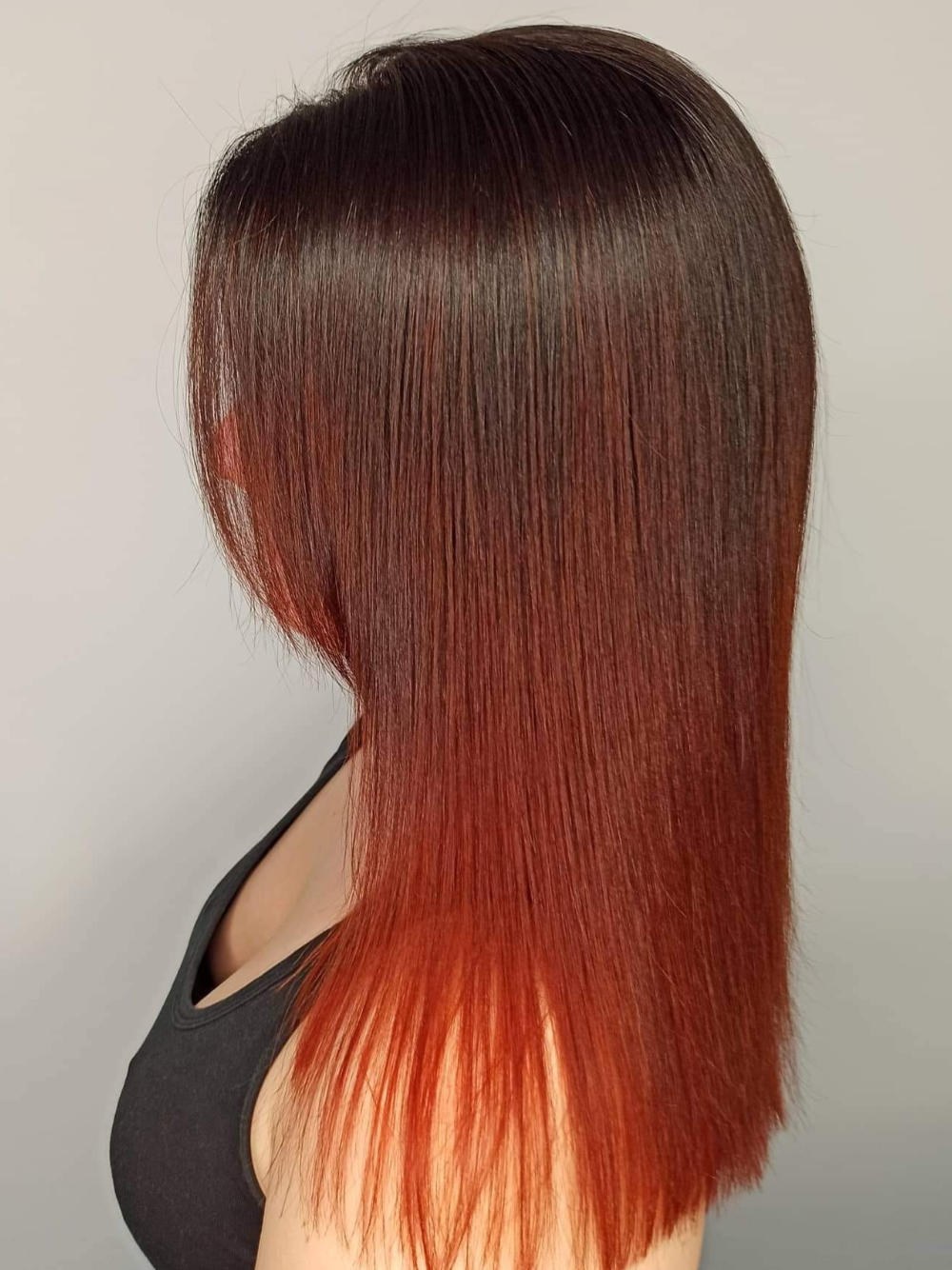 A woman with long brown hair and red highlights is wearing a black tank top.