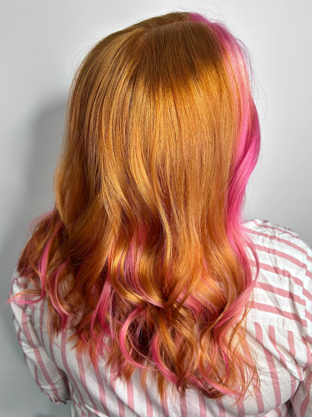 A woman with red hair and pink highlights is wearing a striped shirt.