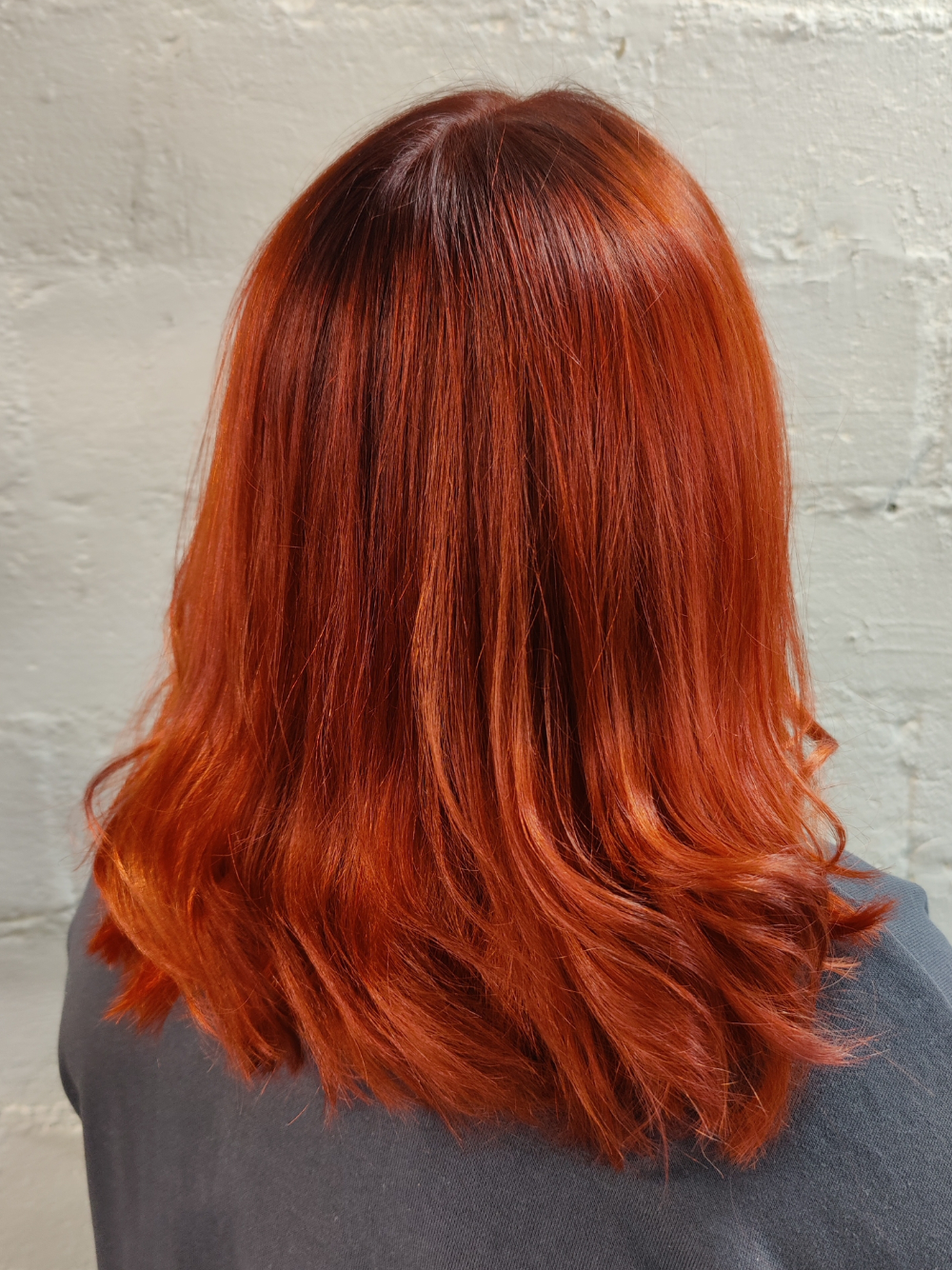 A woman with long red hair is wearing a grey sweater.