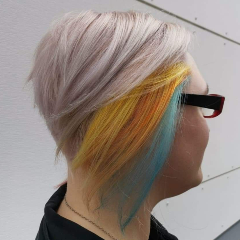 A woman wearing glasses has a rainbow of hair behind her ear