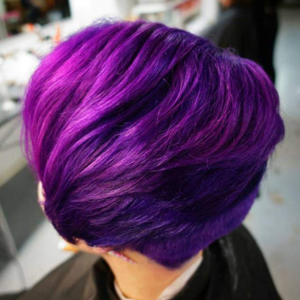 A woman with short purple hair is getting her hair cut.