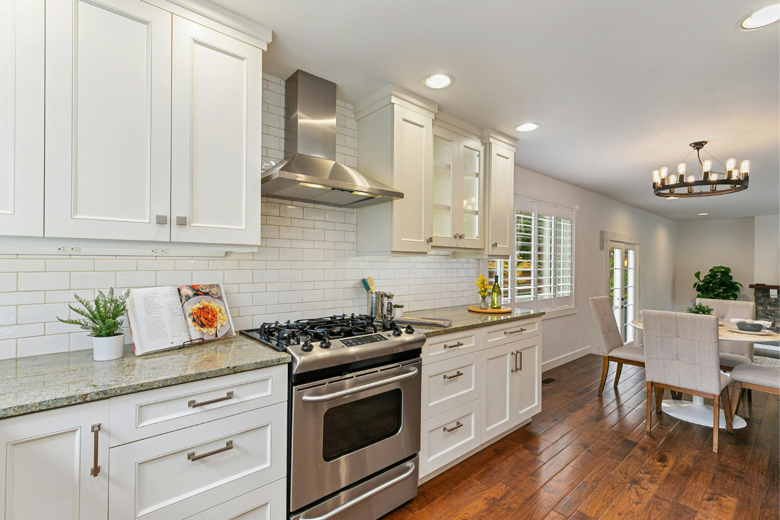 A kitchen with white cabinets , stainless steel appliances , granite counter tops and hardwood floors.