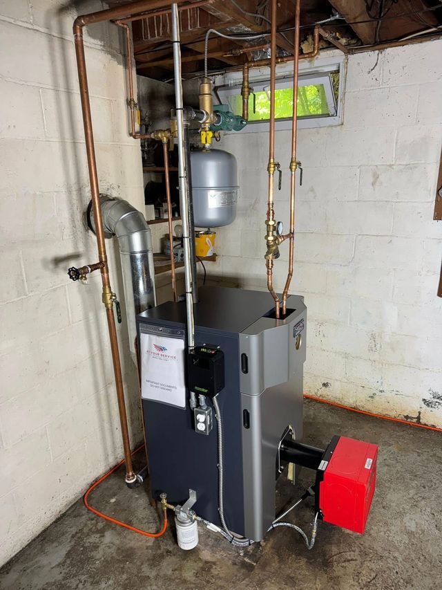 Basement utility room with a boiler, exposed pipes, and a red power vent attached.