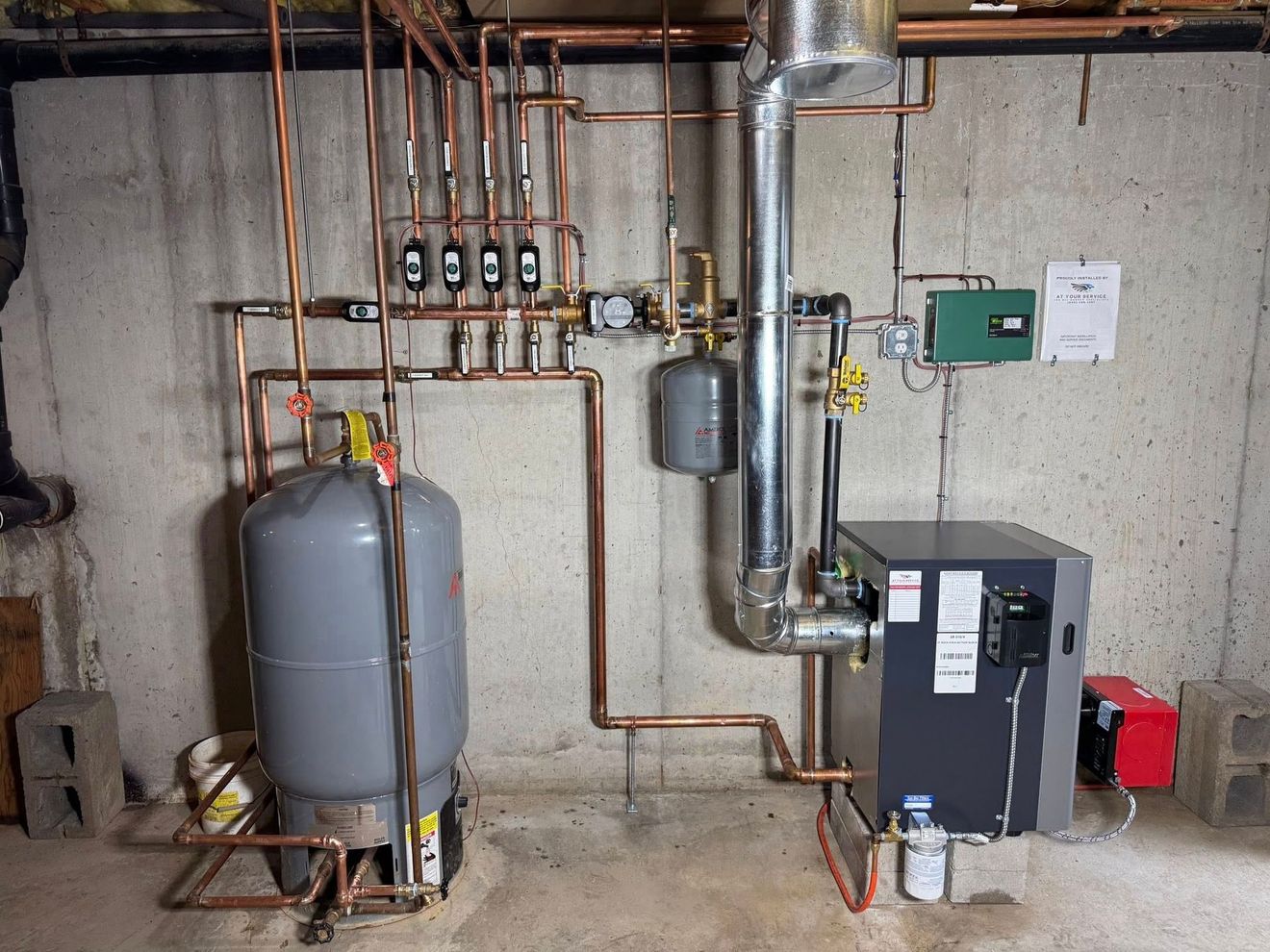 Boiler room with pipes, tanks, gauges, and heating equipment along a concrete wall