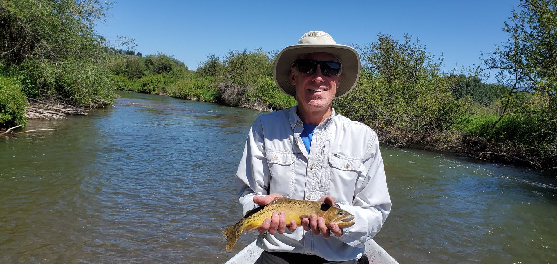 Person in a hat holding a fish in a river under a clear blue sky