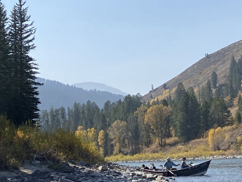 River with people rafting in a forested mountain valley under a clear blue sky