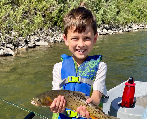Smiling child in a boat holding a fish on a sunny riverbank