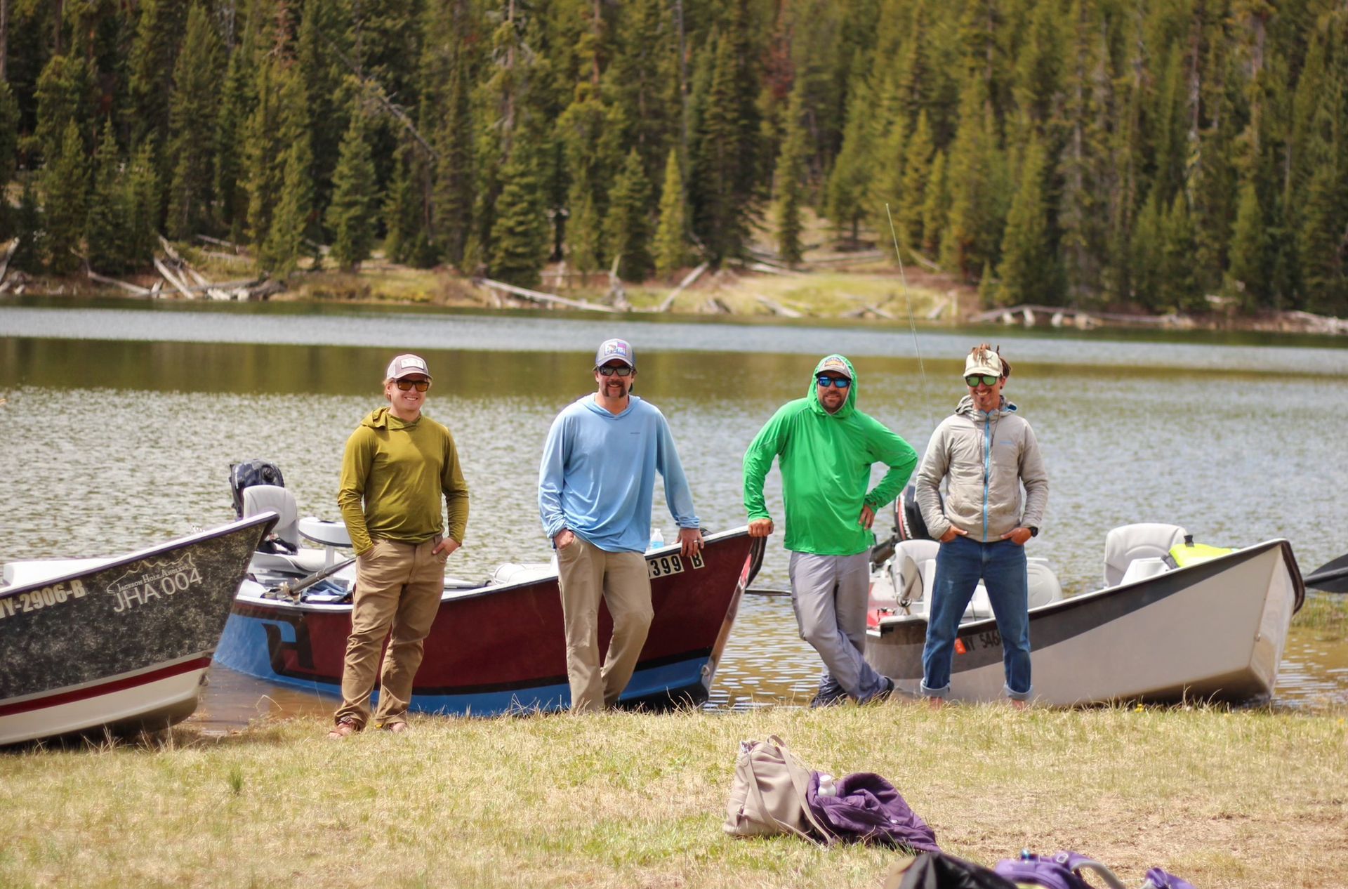 Four people stand by canoes on a lakeshore with forested hills in the background.