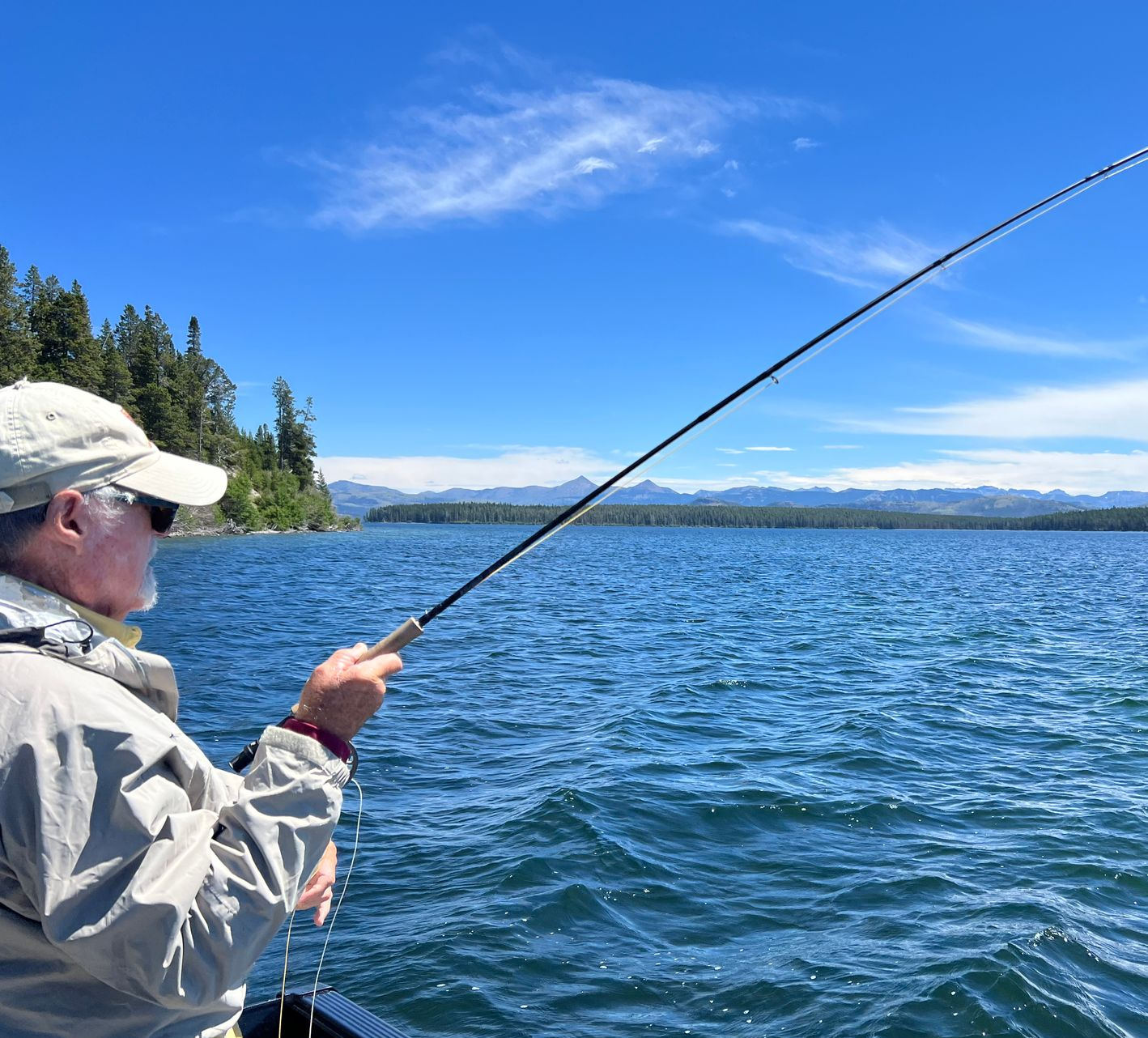 Person fishing from a boat on a blue lake under a clear sky
