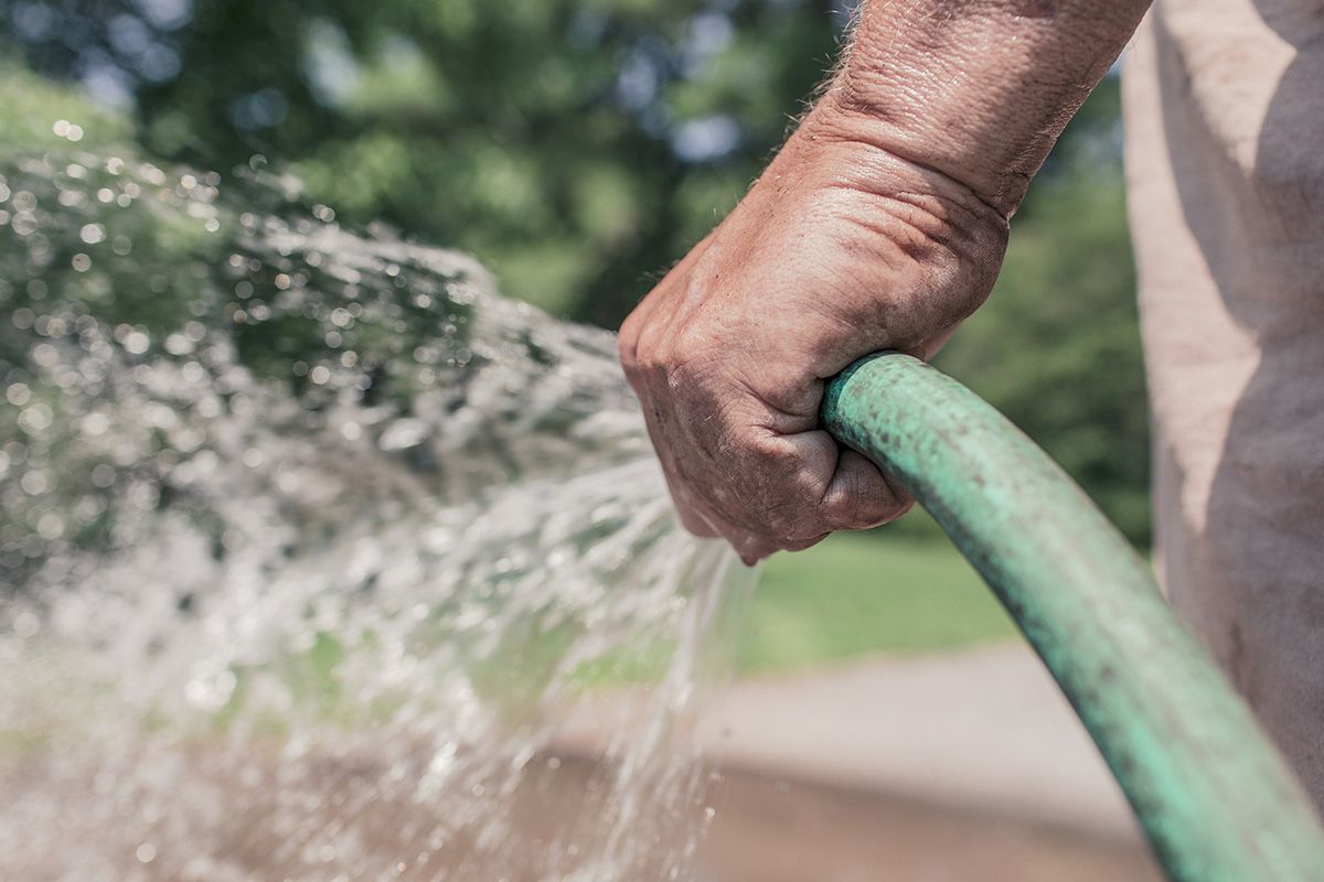 Hand holding a green garden hose, spraying water.