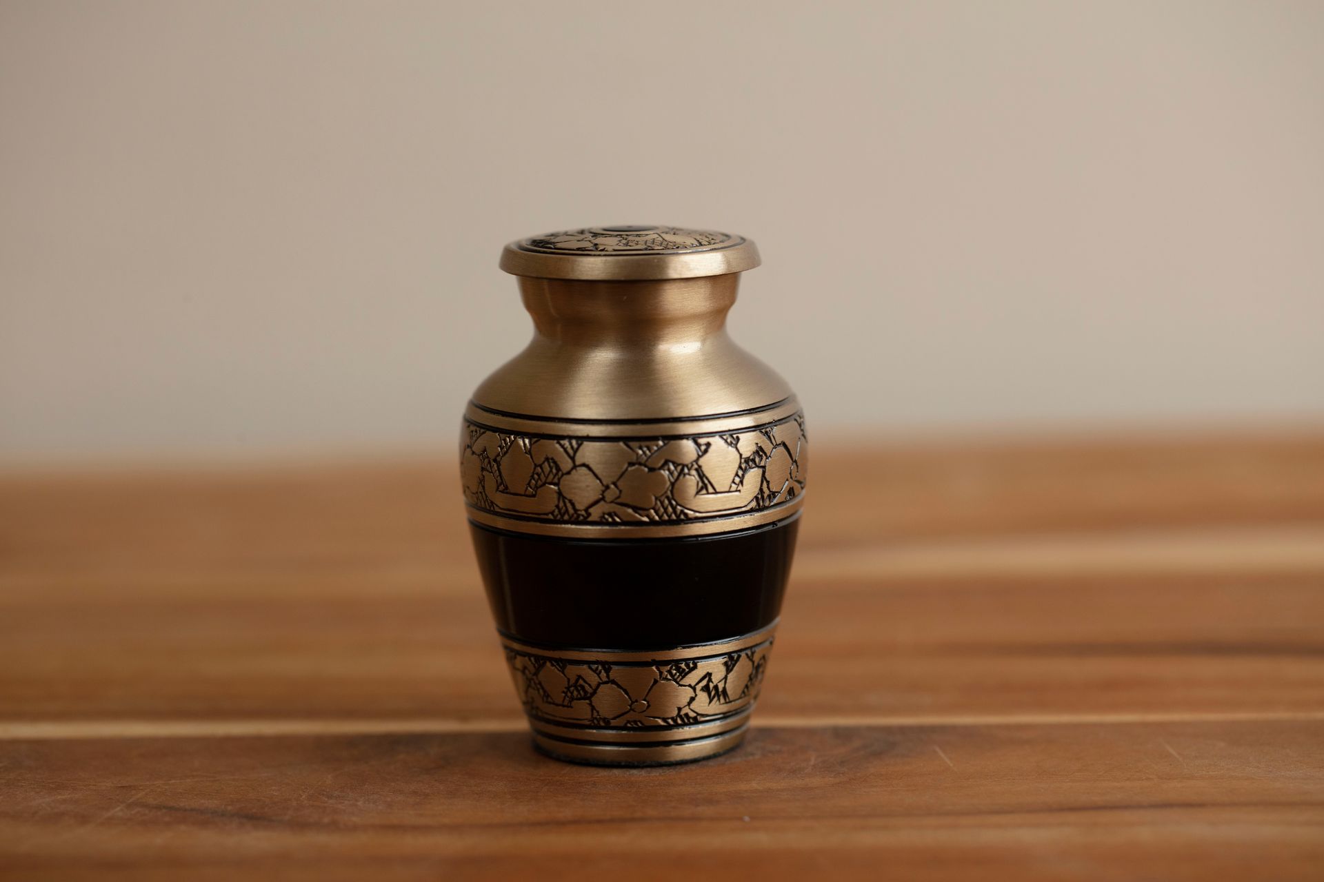 Small gold decorative vase with black bands on a wooden surface