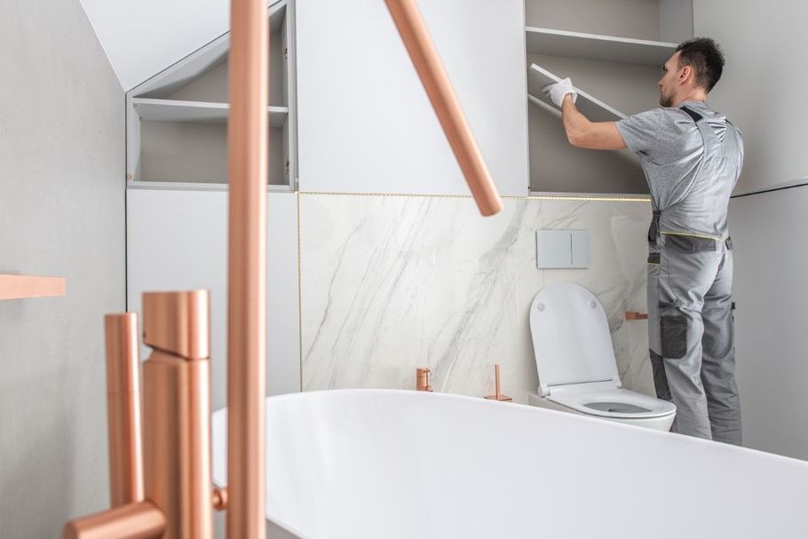 Person painting a gray wall above a toilet in a modern bathroom