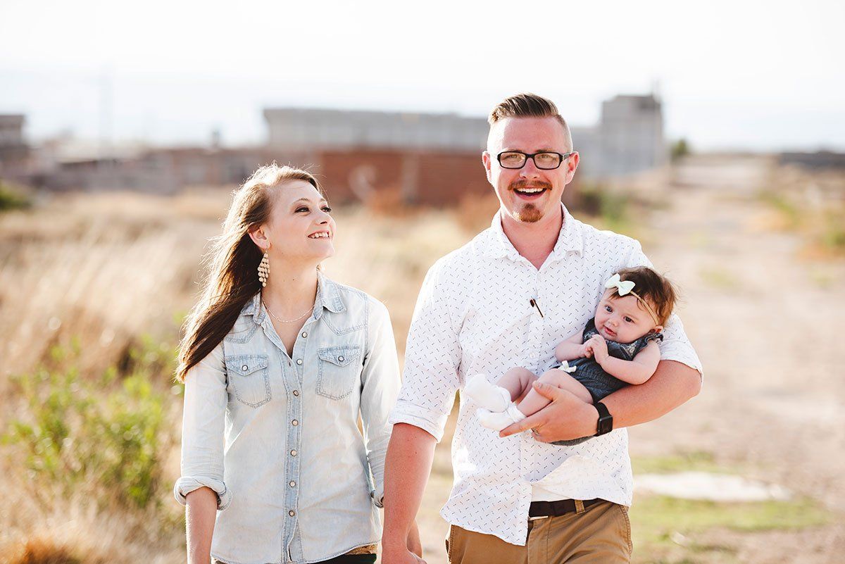 A man and a woman are holding a baby while walking down a dirt road.