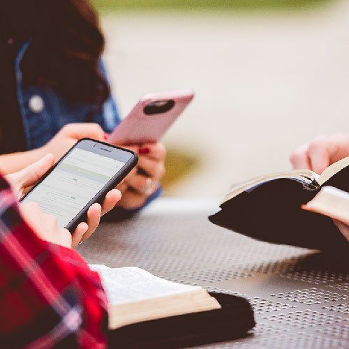 A group of people are sitting at a table with a bible and a cell phone.